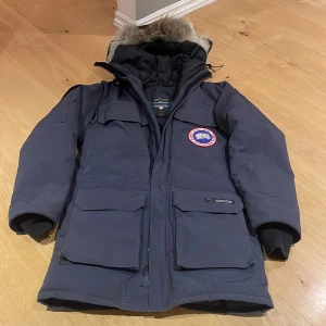 Mörkgrå Canada Goose dunjacka XS - Säljer en mörkgrå Canada Goose dunjacka med stor huva och äkta pälsdetalj. Jackan har flera stora fickor, ribbade muddar och klassisk logga på bröstet. Perfekt för kalla vinterdagar! Storleken motsvarar 36/38 i tjejstorlek. Jackan har några år på nacken med är inte använd de senaste åren. En riktig klassisker!