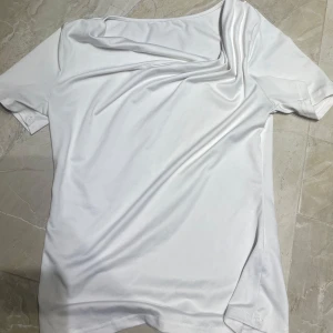 Vit kortärmad t-shirt i polyester - En stilren vit t-shirt med korta ärmar och rund hals. Tillverkad i ett slätt och lätt polyestermaterial som ger en mjuk känsla mot huden. Perfekt för en clean och enkel look.