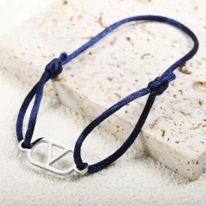 Blått armband med silverdetalj - Snyggt armband med marinblått band och en stilren silverfärgad detalj i form av en geometrisk symbol. Justerbar storlek med knutar på sidorna, perfekt för att ge din outfit en cool touch.