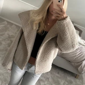 Beige teddyjacka med bred krage - Säljer en supermysig teddyjacka i beige med bred krage och loose passform. Jackan har en fluffig, teddytextur som ger en chill vibe och är perfekt för kyliga dagar. Långärmad och croppad modell som är enkel att styla till jeans eller kjol.