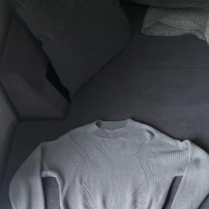 Ljusgrå stickad tröja med mönster - Säljer en ljusgrå stickad tröja med snygga stickade detaljer framtill. Tröjan har rund halsringning och långa ärmar. Perfekt för dig som gillar en enkel men ändå stilren look.