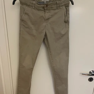 Beige chinos i bomull - Snygga beige chinos med klassisk passform och smalare ben. Byxorna har fickor i sidorna och en enkel knappstängning i midjan. Perfekta för en clean och avslappnad stil. Tillverkade i mjuk bomull som känns skön mot huden. Se defekt på ena låret. 
