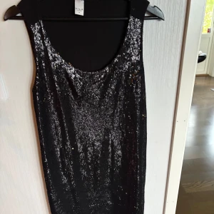 Svart paljettklänning från Vila - Snygg svart kortklänning från Vila med glittriga paljetter framtill. Ärmlös modell med rund halsringning och slät baksida. 