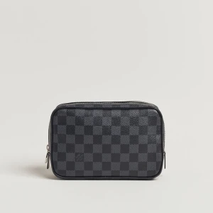 Rutig svart handväska Louis Vuitton - Snygg svart handväska från Louis Vuitton med klassiskt rutigt mönster. Väskan är rektangulär med dragkedja upptill och tillverkad i skinn. Perfekt för att bära dina viktigaste grejer med stil.