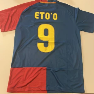FC Barcelona Eto'o 2009 Finaltröja Nike - Säljer en ikonisk FC Barcelona fotbollströja replika från Champions League-finalen 2009 med Eto'o och nummer 9 på ryggen. Tröjan är kortärmad, i blått och rött med gula detaljer, klubbmärke och Nike-logga. Materialet är lätt och andas, perfekt för match eller samling. Endast handtvätt gäller!