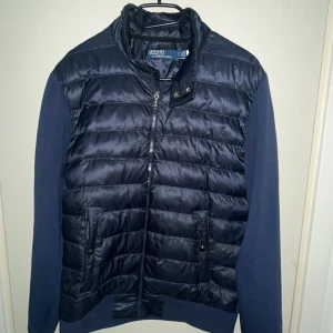 Cardigan Polo Ralph Lauren - Snygg marinblå pufferjacka från Polo Ralph Lauren med quiltad framsida och ärmar i mjuk bomull. Jackan har dragkedja, ståkrage och två fickor framtill. Klassisk broderad logga på ärmen för extra stilpoäng. Pris kan diskuteras vid snabb affär.