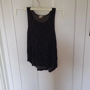 Svart linne från H&M Basic - Säljer ett svart linne från H&M Basic med diskret melerat mönster. Modellen är ärmlös med rund halsringning och lite längre baktill. Perfekt för en avslappnad och sportig look. Materialet är mjukt och lätt, passar bra till varma dagar eller träning.