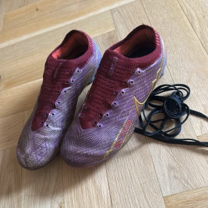 Nike Mercurial fotbollsskor röd/guld - Säljer ett par Nike Mercurial fotbollsskor i vinröd med guldiga detaljer och mönstrad ovandel. NIKE AIR ZOOM MERCURIAL VAPOR 15 ELITE FG MBAPPÉ 