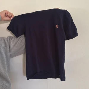 LES DEUX T-shirt - Snygg mörkblå t-shirt med korta ärmar och liten broderad detalj i orange på bröstet. Enkel och stilren design, perfekt till jeans eller shorts. T-shirten är i mjuk bomull och har en klassisk passform.
