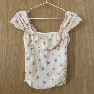 Blommig mesh topp från Gina Tricot - Supersöt topp från Gina Tricot i ljusgul mesh med små rosa blommor. Toppen har breda axelband och lätt rynkade detaljer framtill. 