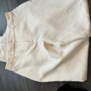 Vita kostymbyxor från Amisu - Stilrena vita kostymbyxor från Amisu i storlek 40. De är högmidjade med bälteshällor och har en klassisk, rak passform. Perfekta för en fräsch och clean look under varmare dagar. Materialet känns mjukt och lätt, vilket gör dem riktigt sköna att bära.