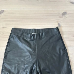 Svart skinnbyxa från NLY Trend - Svart, tight skinnbyxa från NLY Trend i storlek M. Byxorna har en clean look med dragkedja i sidan och är gjord i syntetmaterial som ger en cool läderkänsla. Perfekt för dig som vill ha en edgy vibe till din outfit.