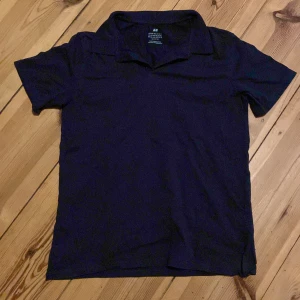 Svart piké t-shirt från H&M - En stilren marinblå piké från H&M i storlek 158/164. Klassisk krage och korta ärmar, perfekt för en clean och enkel look. Passar dig som gillar basic men snygg stil.