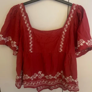 Röd blus med broderi från Old Navy - Superfin röd blus från Old Navy med vita broderade blommor längs ärmar, halsringning och nederkant. Blusen har korta puffärmar och en fyrkantig urringning. 