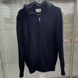 Svart hoodie i kashmir från Soft Goat - Mysig svart hoodie från Soft Goat i 100% kashmir. Tröjan har dragkedja framtill, huva och långa ärmar. Perfekt för dig som gillar en stilren och enkel look med lyxig känsla. Snygg att bära till både jeans och mjukisbyxor. 