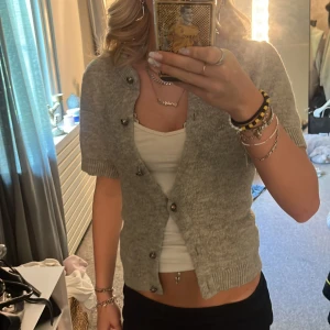 Grå kofta  - Kortärmad grå kofta från Gina Tricot i storlek XS. Koftan är stickad med ribbade muddar och har knappar framtill. Perfekt att slänga över ett linne för en chill och snygg look.