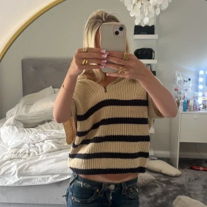 Beige stickad randig tröja med half zip - Superfin beige stickad tröja med svarta ränder och kort ärm. Tröjan är croppad, har en liten half zip vid halsen och kan bäras offshoulder för en chill vibe. Perfekt till jeans eller kjol för en trendig look.