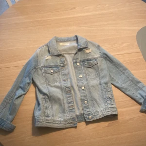 Ljusblå jeansjacka från Madison Denim - Säljer en klassisk ljusblå jeansjacka från Madison Denim i storlek S. Jackan har slitna detaljer vid axlarna, bröstfickor med knappar och silverfärgade knappar framtill. Perfekt oversized vibe och passar till allt. 