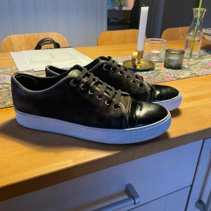 Lanvins - Snygga bruna sneakers från Lanvin med ovandel i mocka och tå i blankt skinn. Skorna har vita, platta sulor och bruna skosnören. Klassisk och stilren design som passar perfekt till jeans eller dressade byxor.