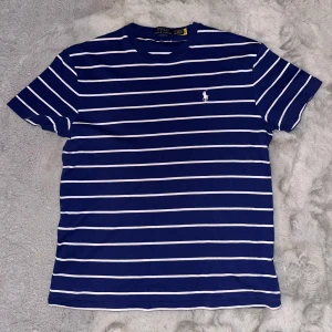Ralph Lauren T-Shirt Med Print - Blå/vit randig. Väldigt gott skick skulle uppskatta att den är använd max 10 gånger. Väldigt mjuk och skön. Tyvärr för liten för mig nu därför säljes den. Storlek S. 100% äkta kvitto finns på sista bilden. Mvh
