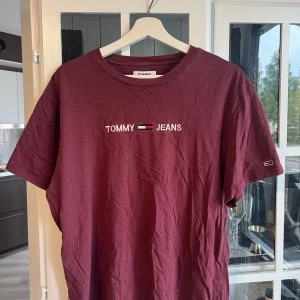 Vinröd t-shirt från Tommy Jeans - Snygg vinröd t-shirt från Tommy Jeans med broderad logga på bröstet och ärmen. Klassisk rund halsringning och korta ärmar. Tillverkad i mjuk bomull som är skön att bära. Perfekt för en chill och stilren look.