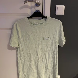 Ljusgrön t-shirt från 157, M - Fräsch ljusgrön t-shirt från 157 i 100% bomull. Klassisk passform med korta ärmar och rund hals. Tryck med texten 'stay local.' på bröstet ger en clean och chill vibe. Perfekt till jeans eller shorts för en enkel och snygg look.