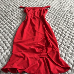 Röd offshoulder klänning från SHEIN - Snygg röd offshoulder klänning från SHEIN med volangdetaljer och omlottkänsla nertill. Klänningen har en figurnära passform, dragkedja bak och är tillverkad i ett mjukt syntetmaterial. Perfekt för dig som vill sticka ut med en färgstark look.