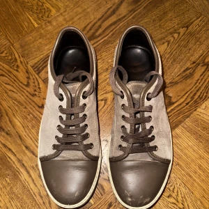 Gråbruna Lanvin sneakers i mocka - Snygga sneakers från Lanvin i beige/grå mocka med bruna skinn-detaljer och tåparti. Skorna har krämfärgad sula och bruna snören, samt diskret branding på sulan. Perfekt för dig som gillar stilrena och exklusiva sneakers med en clean vibe. Storlek 6, vilket sitter som stl 41. Skulle möjligtvis kunna passa 40-40 1/2 också. Priset är aningen förhandlingsbart. Skorna är i bra skick, endast lädret på tåpartiet som fått en liten smäll.