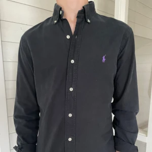 Ralph lauren skjorta  - Säljer dennna riktigt snygga Ralph lauren skjorta i svart som är i mycket bra skick, storlek S modell slim fit, den är 73 cm lång och 45 cm bred under armhålorna, hör gärna av dig vid frågor! 