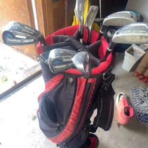 Wilson golfbag med klubbor. - Golfbag från Wilson i svart och rött med flera fack. Perfekt om du är ny till golf då klubborna är väldigt förlåtande. Det är dam klubbor vilket betyder att skaftet är lite mjukare, vilket passar en nybörjare perfekt. Pris kan diskuteras.
