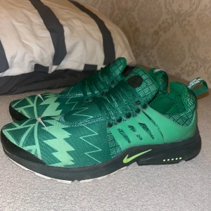 Gröna Nike Presto sneakers med mönster - Nike Presto sneakers i grönt med grafiskt mönster och svarta detaljer. Ovandelen är i textil med coola zigzag- och rutmönster, och sidorna har genomskinliga gröna plastdetaljer. Sulan är svart med limegröna accenter och vit undersida. Perfekta för dig som vill sticka ut.