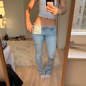Ljusblå slitna bootcut jeans - Säljer ett par ljusblå jeans med låg midja och bootcut passform. Sydda till lowwaist och hålen är gjorda själv!! Midjemått 36 men det är stretchigt material