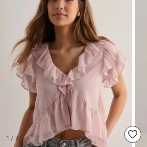 Ljusrosa volangblus från Nelly - Säljer en söt ljusrosa blus från Nelly med volangdetaljer längs ärmar, halsringning och nederkant. Blusen har korta ärmar och knäppning framtill. Tunt, luftigt material som ger en romantisk känsla. Använt 2-3 ggr men finns nån lös tråd och en mindre fläck.