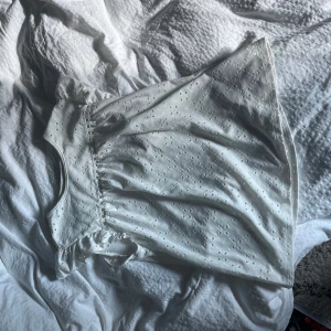 Vit kort klänning med broderade detaljer - Supersöt vit kortklänning med broderade blommor och volang vid axlarna. Ärmlös modell i luftig bomull, perfekt för varma dagar. Snygg och enkel att styla med sneakers eller sandaler.