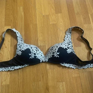 Intimismi spets-bh push up - Supersnygg svart bh med vadderade kupor och vita blommiga spetsbroderier längs kanterna och axelbanden. Axelbanden är justerbara och bh:n har en elegant och feminin look. Perfekt för dig som gillar detaljer och kontraster.