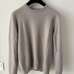 Beige stickad tröja John Henric L - Säljer en stilren beige stickad tröja från John Henric i storlek L. Tröjan har rund halsringning, ribbade muddar och lång ärm. Perfekt för lager-på-lager och enkel att matcha med jeans eller chinos.