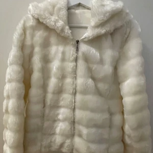 Vit pälsjacka - Fluffig och supermjuk vit pälsjacka med huva och dragkedja framtill. Jackan har en oversized känsla och är perfekt för kalla dagar när du vill vara både varm och stylish. Den har långa ärmar och ett coolt, quiltat mönster i pälsen. Har två fixckor.