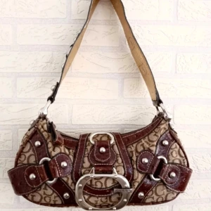 Guess vintage bag<3 - Cool axelväska från Guess med brunt GG-mönster, detaljer i blankt mörkbrunt skinn och stora silverspännen. Insidan av axelbandet är i guldigt, ormskinnsmönstrat material. Väskan har flera nitar och ett stort metallspänne framtill. Perfekt för dig som gillar statement-accessoarer. Kom gärna privat för frågor eller pris förslag!!☺️