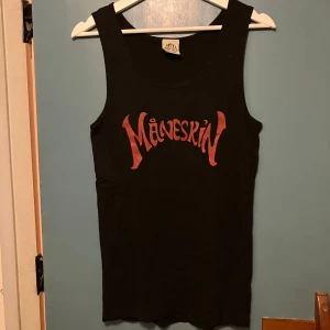 Svart Måneskin linne topp - Säljer ett svart linne med rött Måneskin-tryck framtill. Officiell merch med klassisk rak passform och breda axelband. Perfekt för dig som vill visa din kärlek till bandet och ha en cool, enkel stil. Står XL men passar M/L