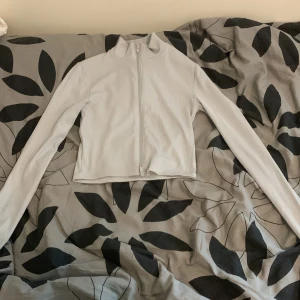 Ljusgrå ribbad tröja från FB Sister - Säljer en ljusgrå ribbad tröja från FB Sister. Tröjan har en dragkedja framtill och långa ärmar. Perfekt för en stilren look. Tillverkad i polyester och elastan för en bekväm passform.