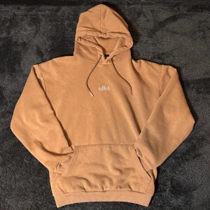 Vintage Hoodie - Säljer en brun hoodie med en liten broderad text på bröstet. Den har en klassisk känguruficka och justerbar huva med dragsko. Perfekt för en avslappnad stil. Tröjan är i storlek: M och har cropped passform.