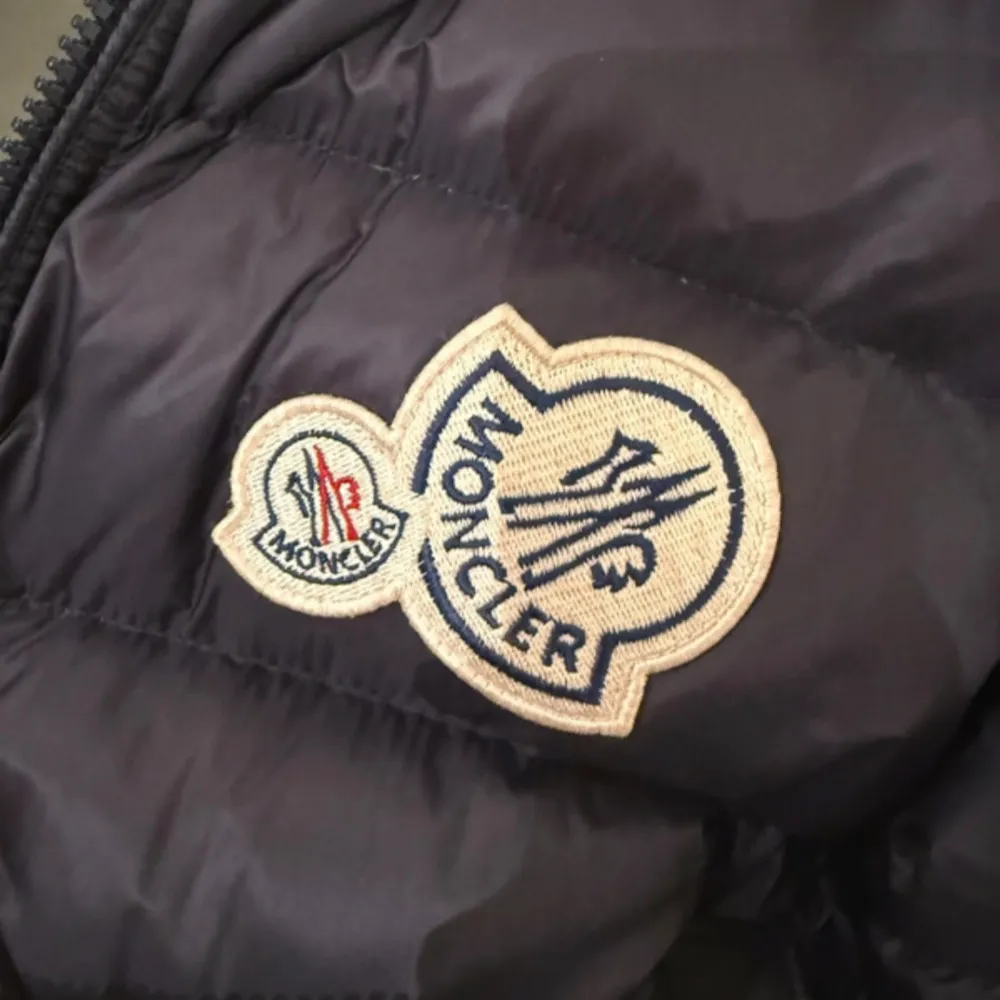 Säljer en snygg svart dunjacka från Moncler med gröna detaljer. Jackan har en dragkedja framtill och en broderad Moncler-logga på bröstet. Perfekt för kyliga dagar med sin quiltade design och långa ärmar.. Takit.