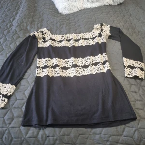 Intimissimi Svart tröja med spetsdetaljer - Snygg svart topp från intimissimi med vackra spetsdetaljer i vitt. Toppen har långa ärmar och en offshoulder-design som ger en elegant look. Perfekt för att lyfta vilken outfit som helst. Den är I väldigt väldigt fin skick. 