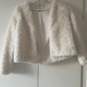 Vit pälsjacka från H&M - Säljer en fluffig och stilren vit pälsjacka från H&M. Jackan har en öppen design utan knäppning och är perfekt för att hålla sig varm och trendig. Den har långa ärmar och en mjuk känsla som ger en lyxig look. Perfekt för kyligare dagar eller speciella tillfällen.