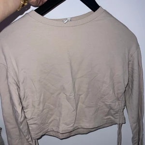Beige croppad tröja med knyt - Säljer en beige croppad tröja med knyt i sidorna. Tröjan har långa ärmar. Från Nelly.