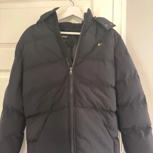 Svart dunjacka från Lyle & Scott -  Storleken är 15-16 years men du kan ha den i 12-15 åldern också. den är perfekt för kyligare väder. Den är vadderad och ger bra värme den är testad på 2 gånger köpte den för 1100kr.