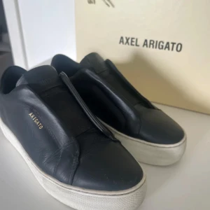 Svarta sneakers från Axel Arigato - Snygga svarta sneakers från Axel Arigato med en stilren design. Skorna har en vit sula och är tillverkade i skinn. Perfekta för en trendig look.