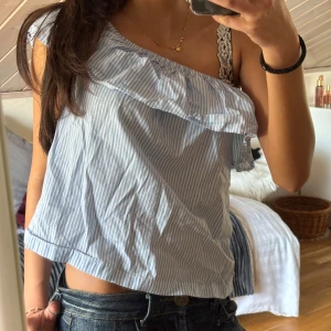 Blå- och vitrandig offshoulder topp - Säljer en söt blå- och vitrandig offshoulder topp med volangdetalj. Perfekt för sommardagar och ger en avslappnad men stilren look. Passar bra till jeans eller kjol för en casual outfit.