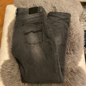 Grå/Svarta Nudie Jeans - Snygga grå jeans från Nudie Jeans. Perfekta för nästan alla klädstilar. Matchar med allt rent sagt. Väldigt ren baksida. Har använt runt 7 ggr sen dem köptes i butik. Dm för minsta fråga! Byte går även, kom med förslag!