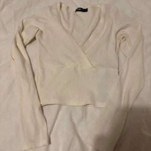 Vit ribbad omlottopp - Säljer en stilren vit ribbad omlottopp från New yorker. Toppen har långa ärmar och en omlottdesign som ger en elegant look. Perfekt för att matcha med både jeans och kjol.